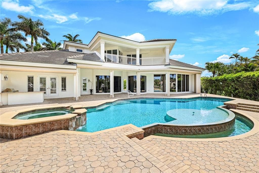 Rear view of house featuring a balcony, a patio area, french doors, a pool with connected hot tub, and a tiled roof