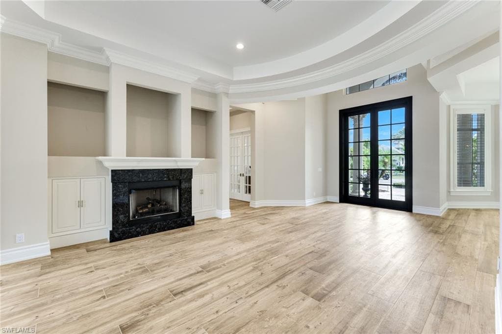 Unfurnished living room with a premium fireplace, light wood finished floors, a raised ceiling, crown molding, and recessed lighting