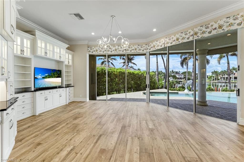 Expansive Family Room room with light wood-style flooring, custom built in cabinetry, a chandelier, crown molding, and recessed lighting overlooking pool, deck and bay.