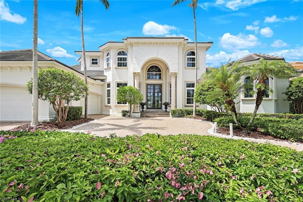 View of front of home with stucco siding, massive French Doors and lush landscaping.