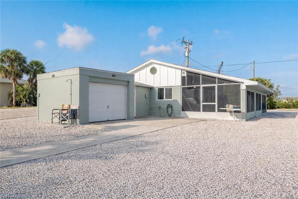 View of back of property featuring an attached garage, driveway, a sunroom, and board and batten siding
