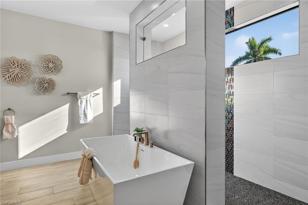 Bathroom with a soaking tub, wood finish floors, and tile walls