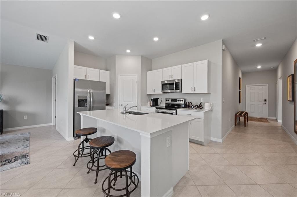 Kitchen with stainless steel appliances, a breakfast bar, light tile patterned floors, a kitchen island with sink, and recessed lighting