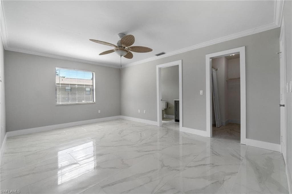 Unfurnished bedroom with a walk in closet, light marble finish floors, crown molding, a closet, and a ceiling fan