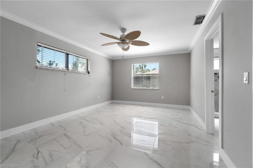 Unfurnished room featuring plenty of natural light, ornamental molding, a ceiling fan, and light marble finish floors