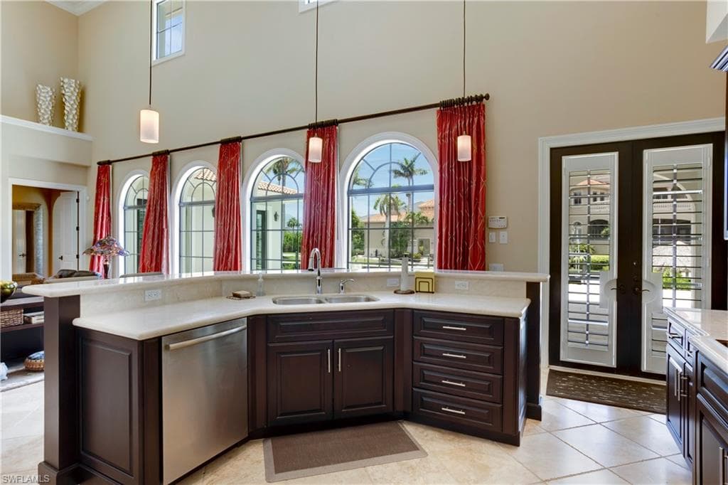 Kitchen with stainless steel dishwasher, a towering 22 ft ceiling, light marble countertops, soft close cabinetry, and decorative light fixtures