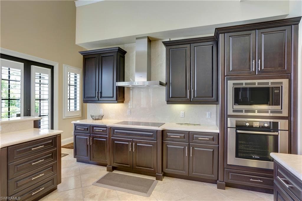 Kitchen featuring appliances with stainless steel finishes, wall chimney exhaust hood, light marble countertops, and plenty of natural light