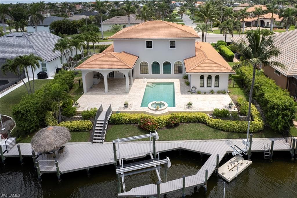 Rear view of house featuring a tiled roof, boat lift, a water view, fenced yard and a patio area