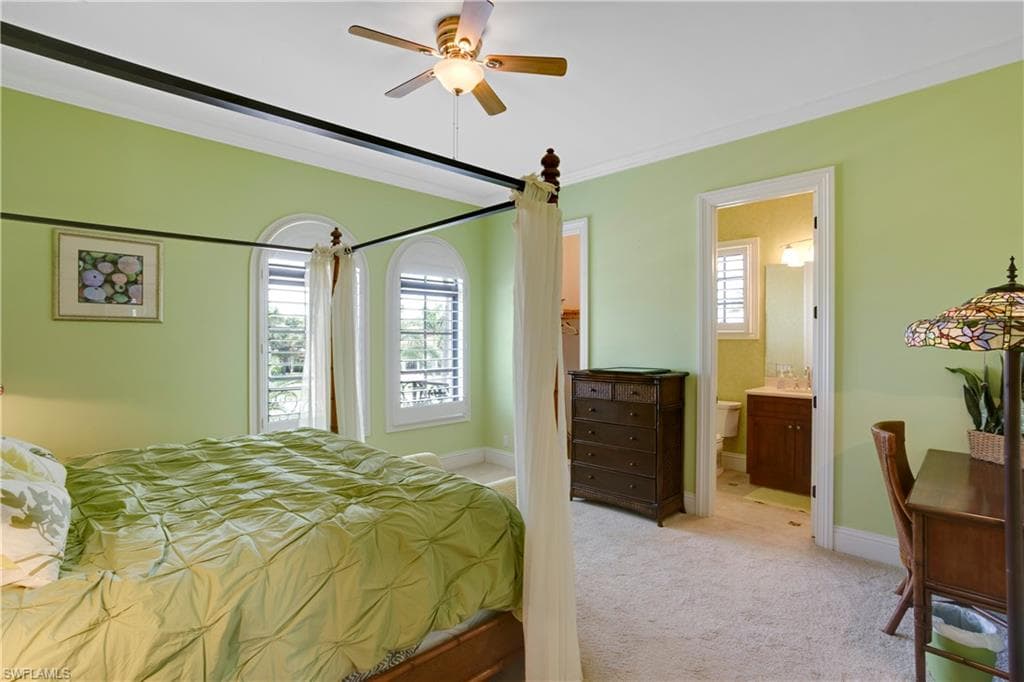 Bedroom with light colored carpet, crown molding, and ensuite bath