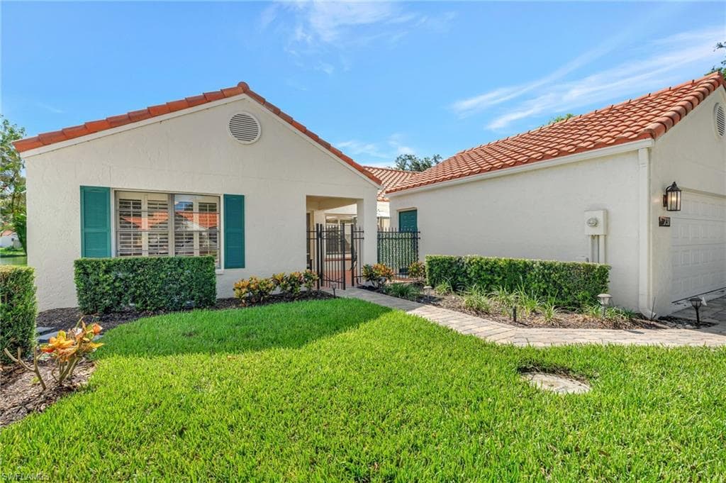 View of front of property featuring a tiled roof, a gate, a front yard, a garage, and stucco siding