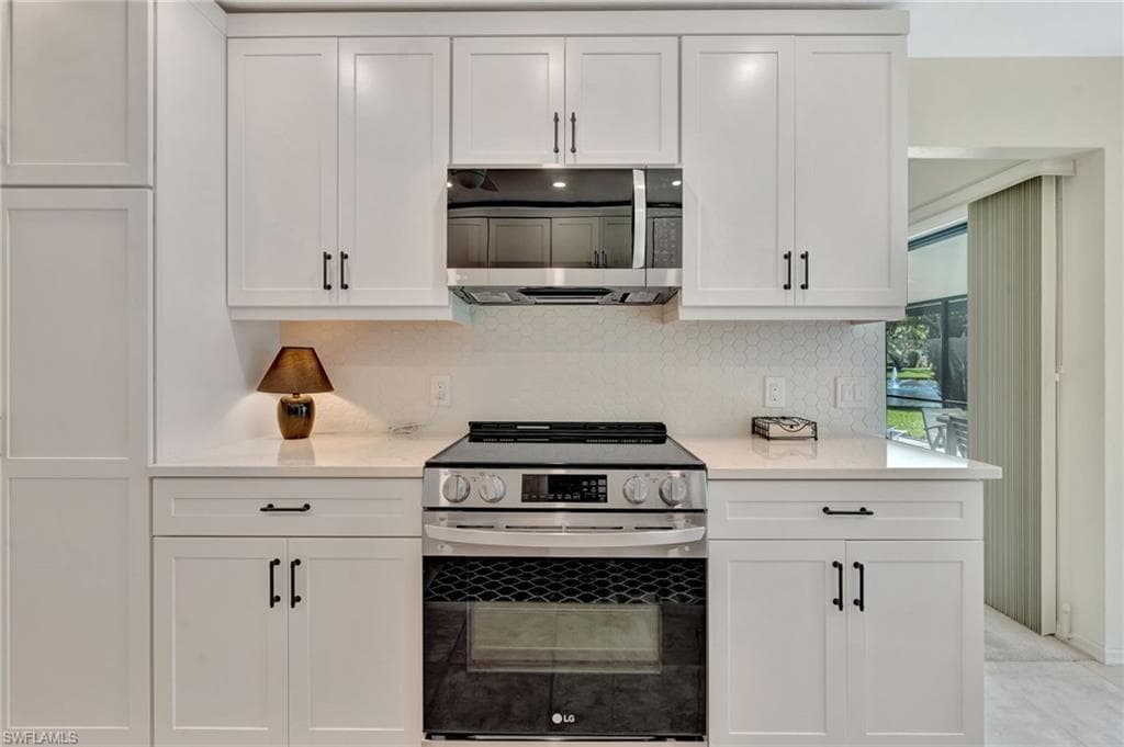 Kitchen featuring stainless steel appliances, white cabinetry, light countertops, and backsplash