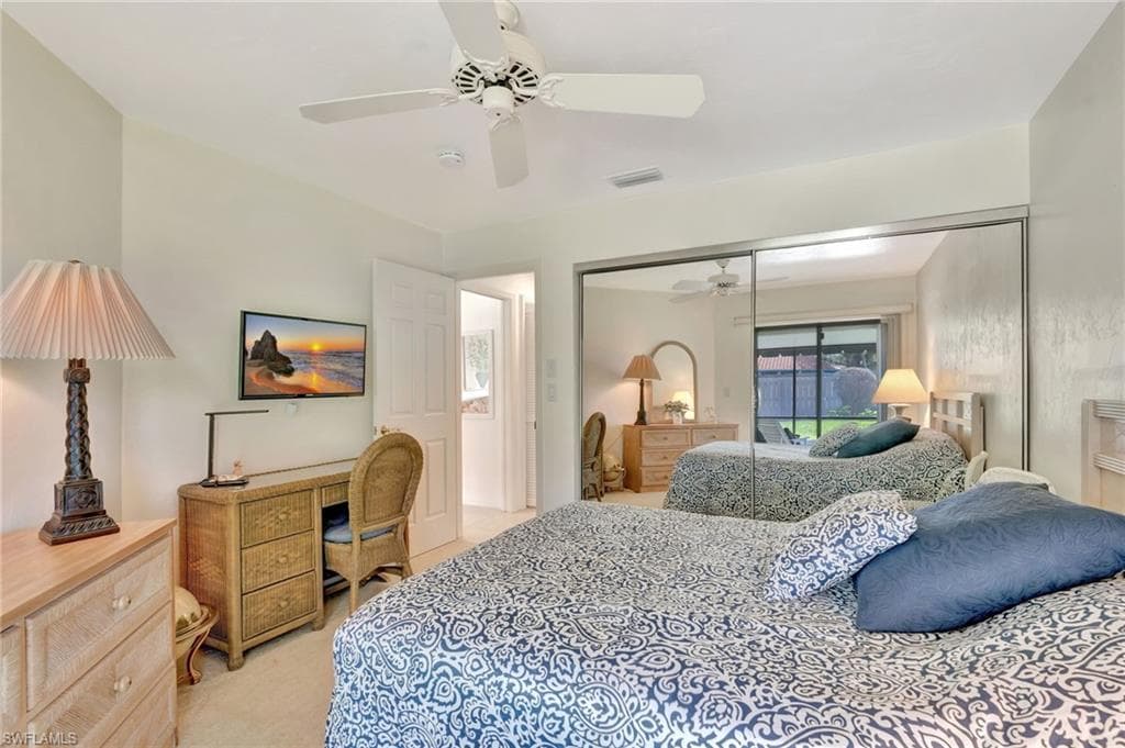 Bedroom with an office area, a ceiling fan, light colored carpet, and a closet