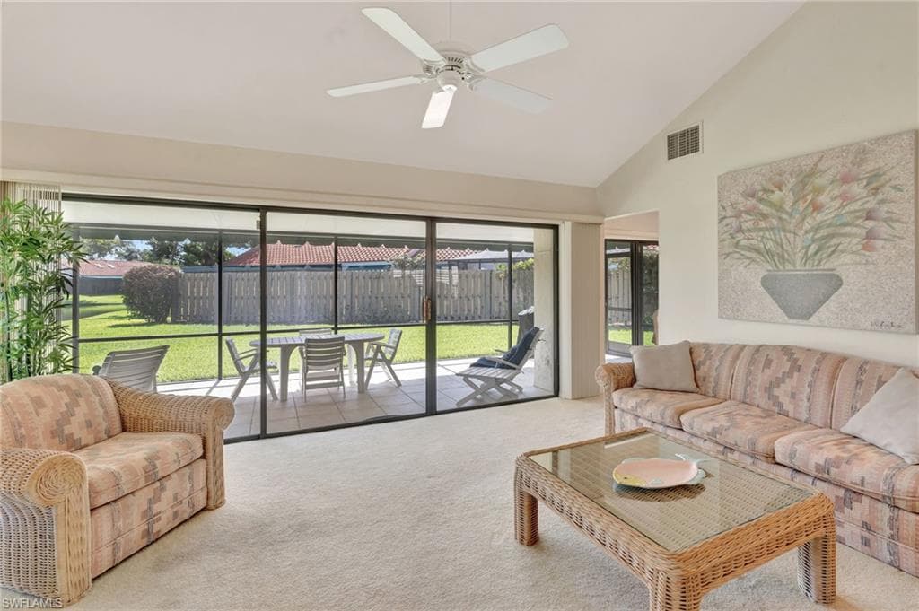 Carpeted living room with ceiling fan, plenty of natural light, and high vaulted ceiling