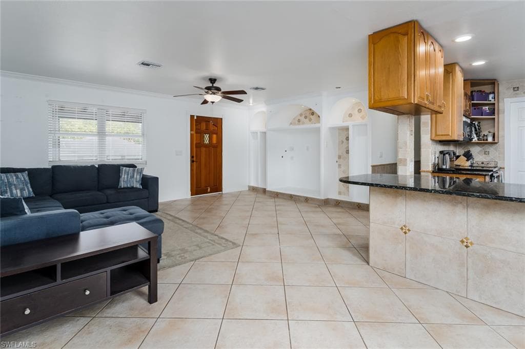 Living area with light tile patterned floors, ceiling fan, and ornamental molding