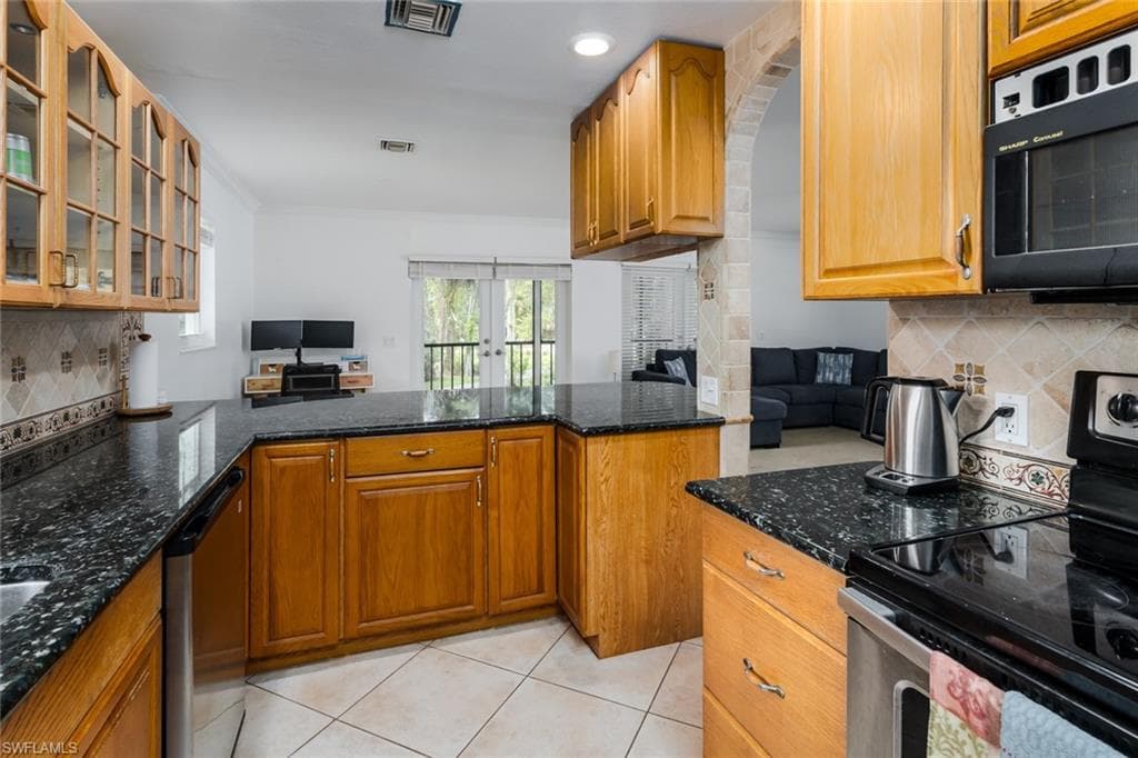 Kitchen featuring stainless steel appliances, open floor plan, glass insert cabinets, dark stone countertops, and decorative backsplash