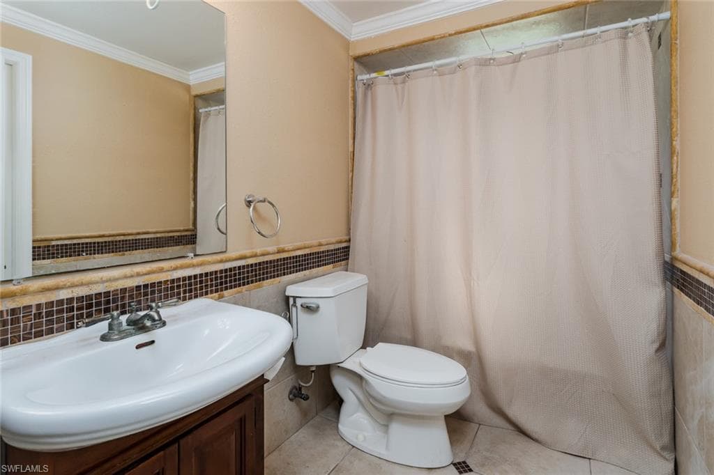 Full bathroom with crown molding, vanity, tile patterned floors, a shower with curtain, and tile walls