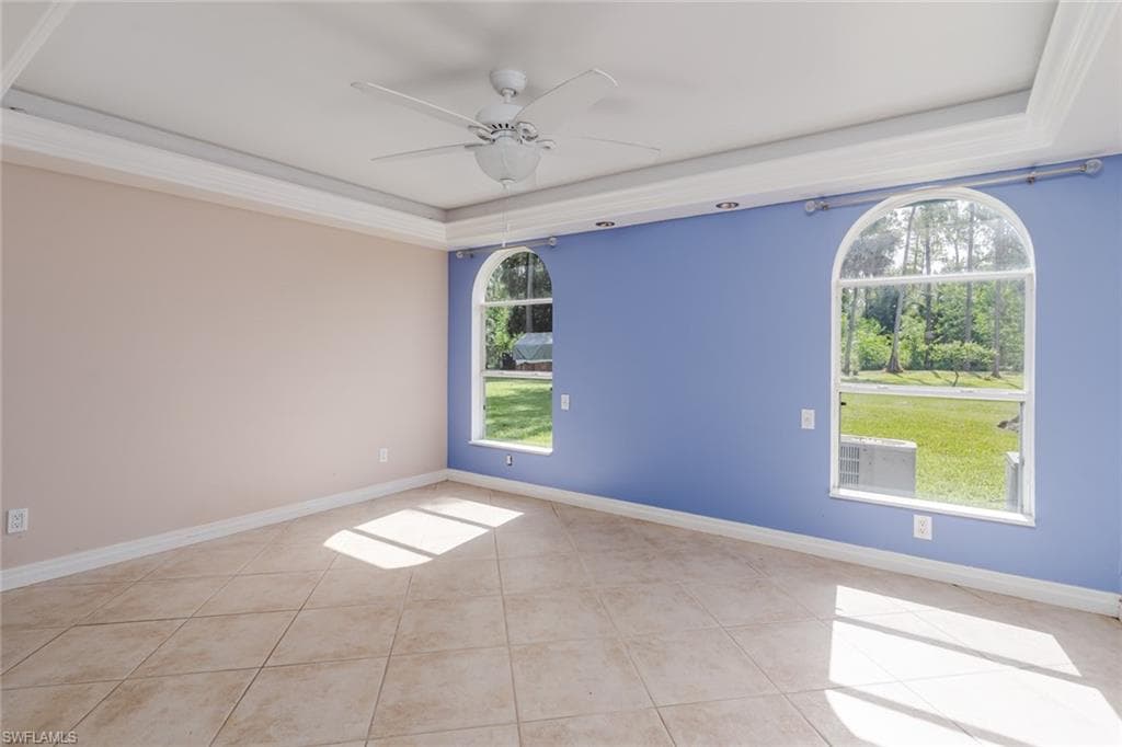 Empty room featuring a tray ceiling, plenty of natural light, ceiling fan, and light tile patterned flooring