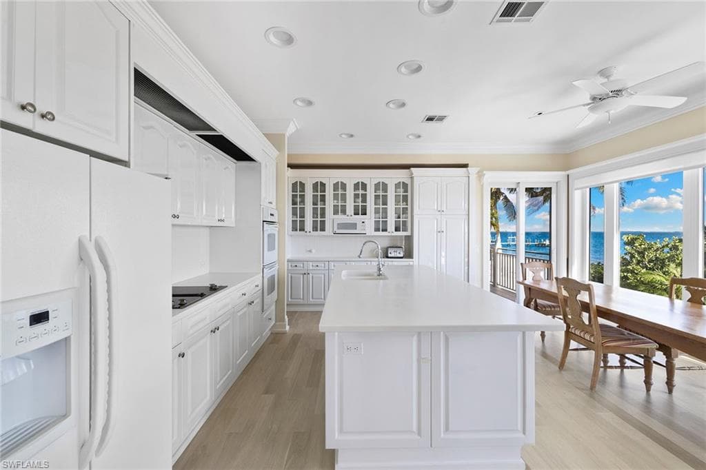 Kitchen with white appliances, glass insert cabinets, white cabinetry, light wood-style floors, and crown molding