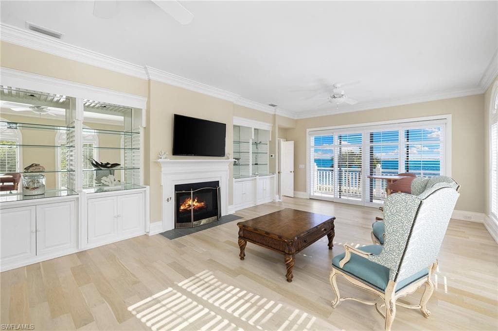 Living area with a ceiling fan, crown molding, light wood-style flooring, and a fireplace with flush hearth