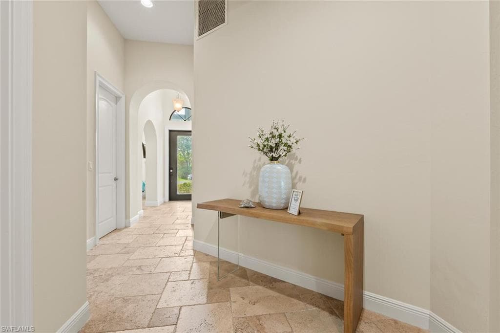 Hall featuring stone tile floors, arched walkways, and recessed lighting