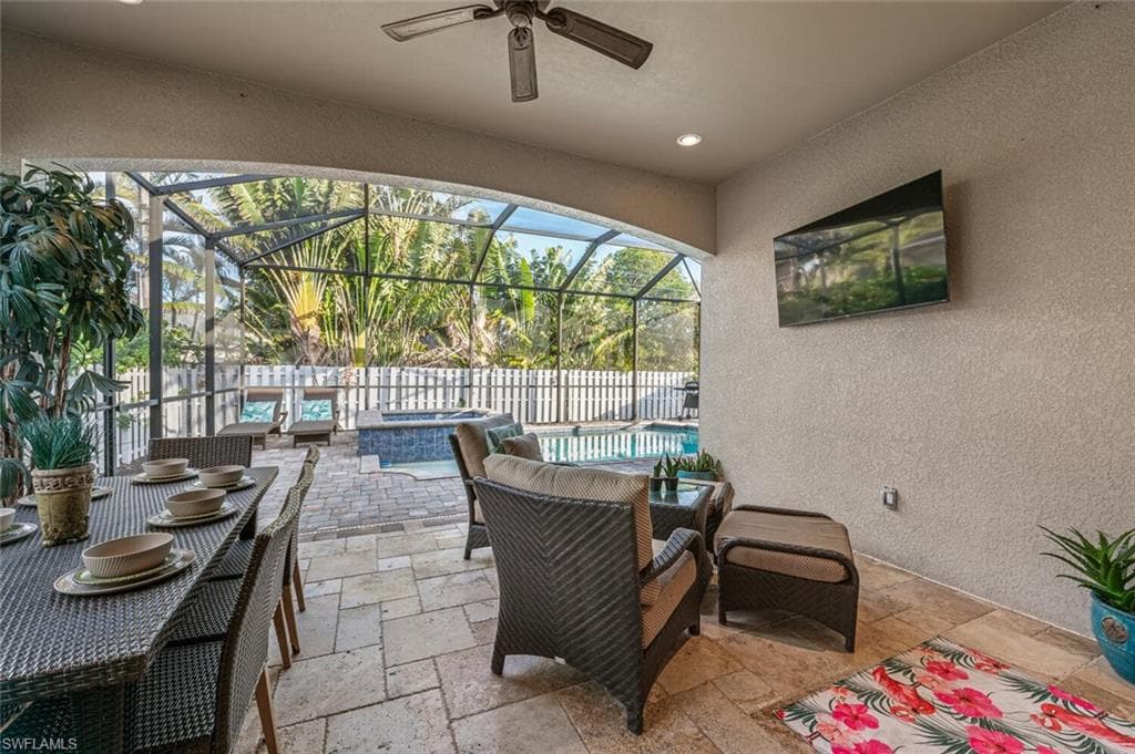 View of patio featuring ceiling fan, a pool with connected hot tub, glass enclosure, and an outdoor hangout area