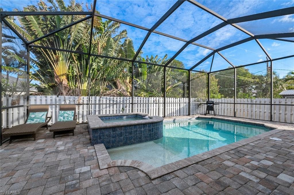 View of swimming pool with a patio area, a pool with connected hot tub, glass enclosure, and a fenced backyard