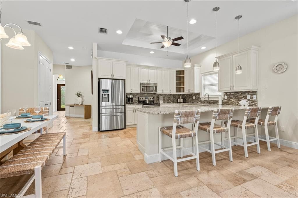 Kitchen with stone tile flooring, backsplash, stainless steel appliances, ceiling fan, and recessed lighting