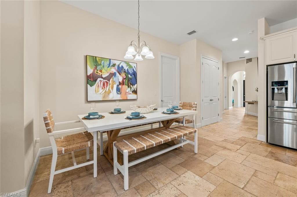 Dining space featuring arched walkways, stone tile flooring, a chandelier, and recessed lighting