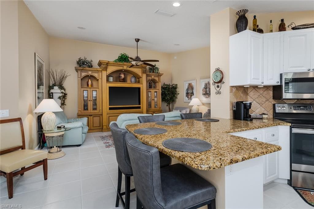 Kitchen featuring a kitchen bar, light stone countertops, a peninsula, decorative backsplash, and open floor plan