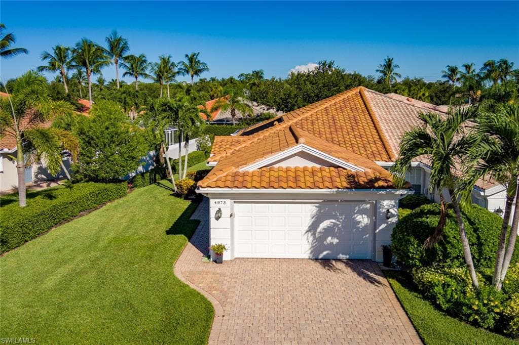 View of front of home with a tile roof, a front lawn, an attached garage, decorative driveway, and stucco siding
