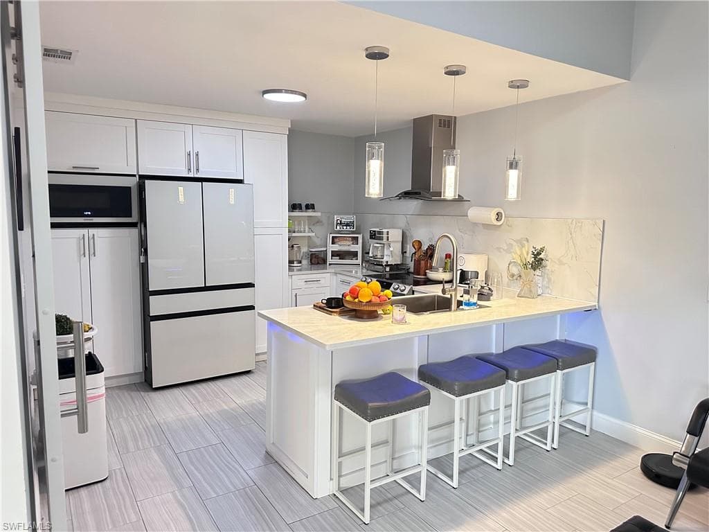 Kitchen featuring a kitchen bar, light countertops, freestanding refrigerator, hanging light fixtures, and range hood