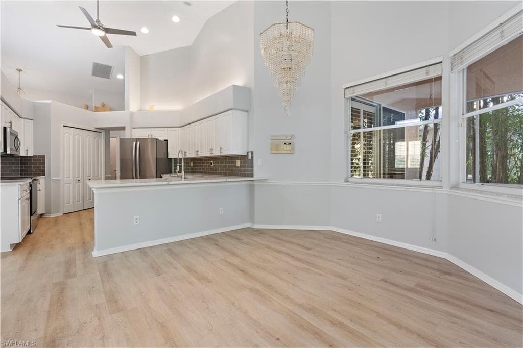 Kitchen with white cabinetry, ceiling fan, appliances with stainless steel finishes, a high ceiling, and light wood-style flooring