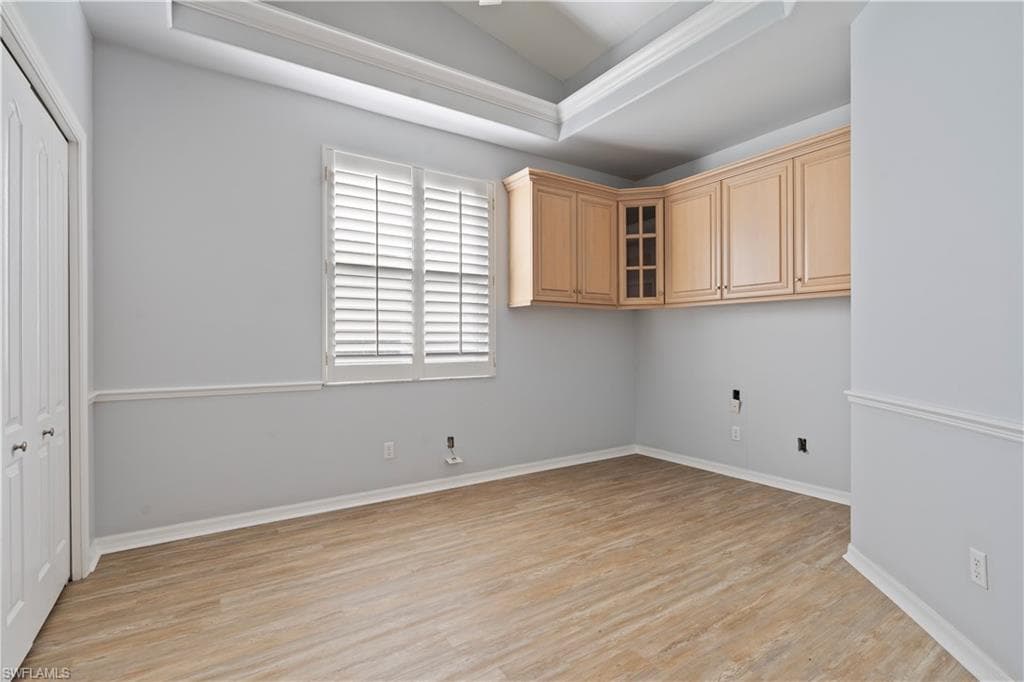 Laundry room featuring vaulted ceiling, light wood-style flooring, and a raised ceiling