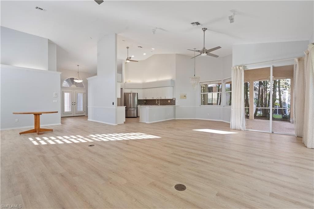 Unfurnished living room featuring french doors, light wood-style flooring, ceiling fan, and high vaulted ceiling
