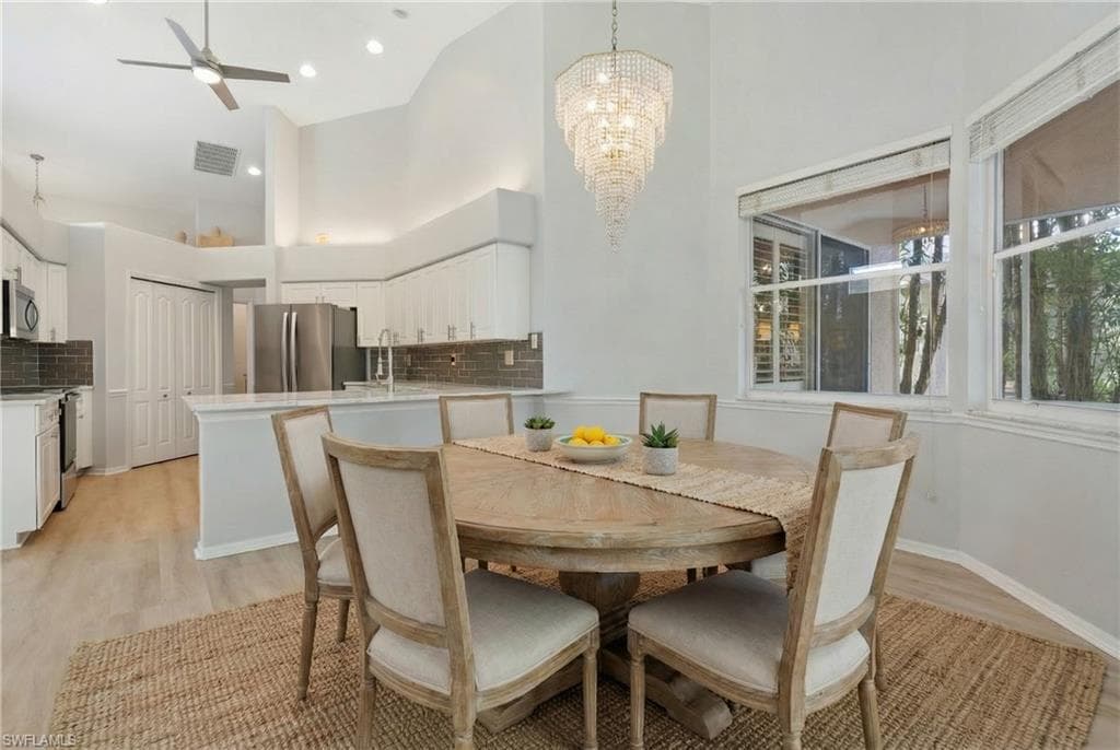 Dining area featuring a ceiling fan, a towering ceiling, a chandelier, and light wood-style flooring