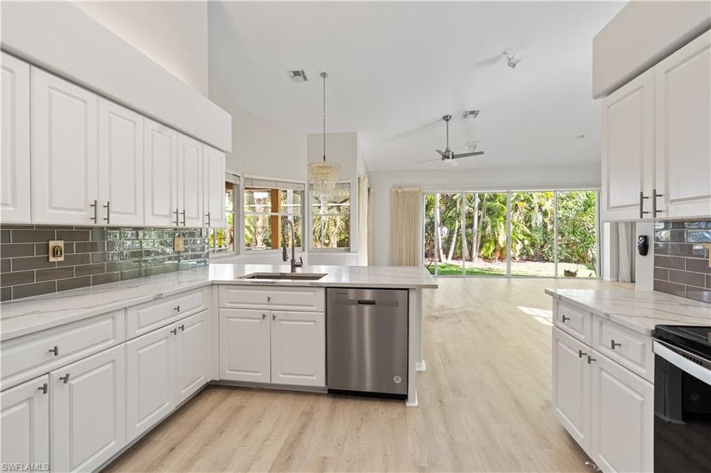 Kitchen with tasteful backsplash, white cabinets, dishwasher, light stone counters, and vaulted ceiling
