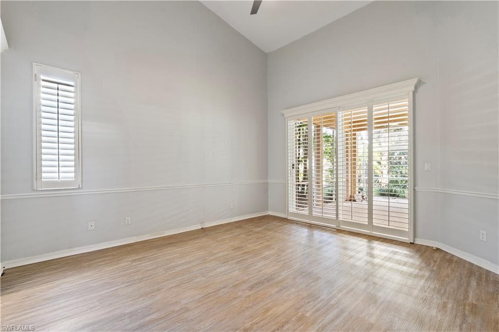 Empty room featuring light wood finished floors, ceiling fan, and high vaulted ceiling