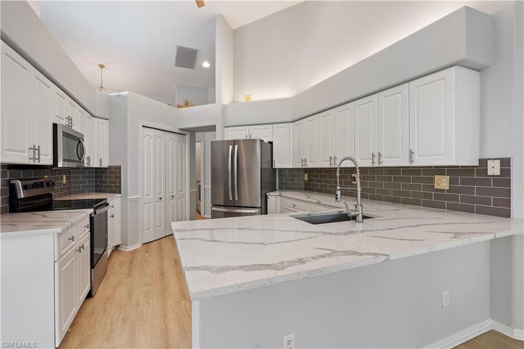 Kitchen with appliances with stainless steel finishes, light stone counters, and white cabinetry