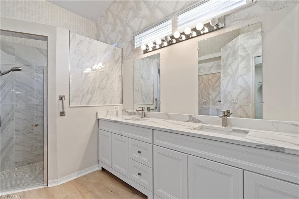 Bathroom with a marble finish shower, double vanity, and light wood-type flooring