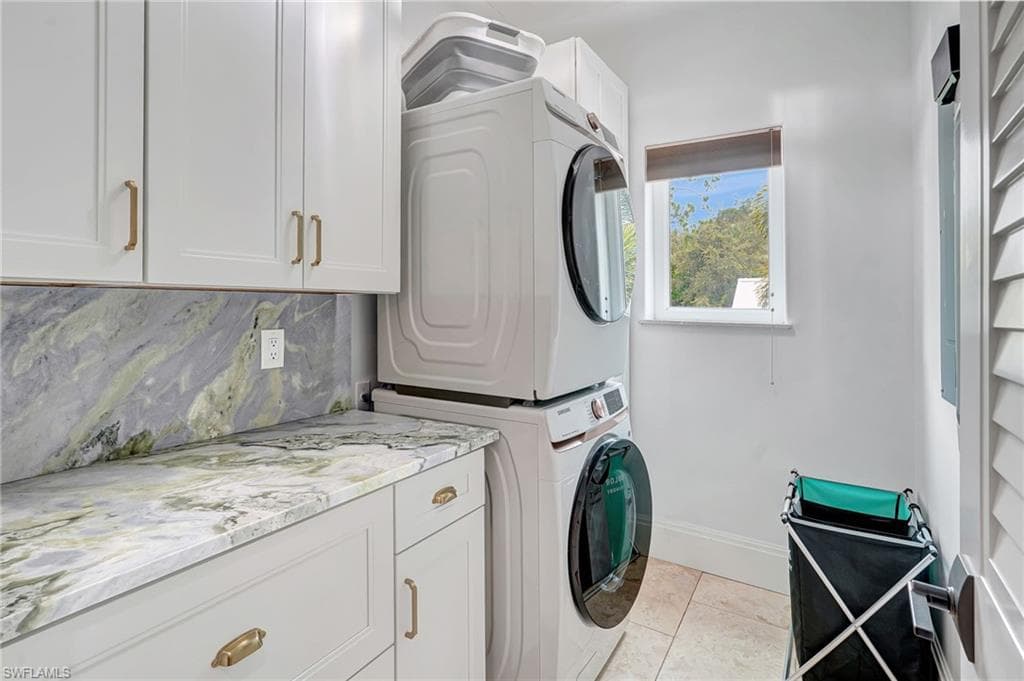 Laundry room featuring cabinet space, stacked washer / dryer, and light tile patterned flooring