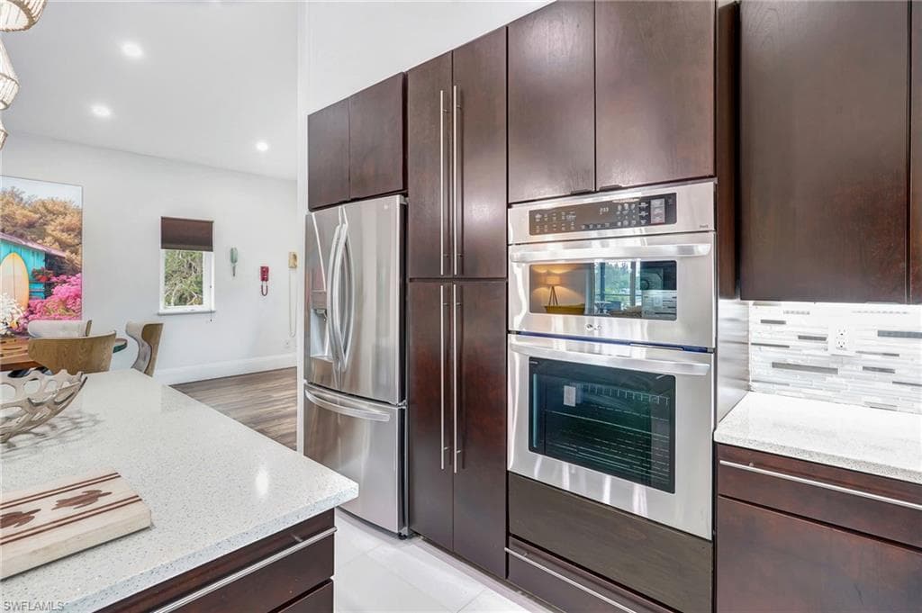 Kitchen featuring dark brown cabinetry, appliances with stainless steel finishes, light stone countertops, recessed lighting, and tasteful backsplash