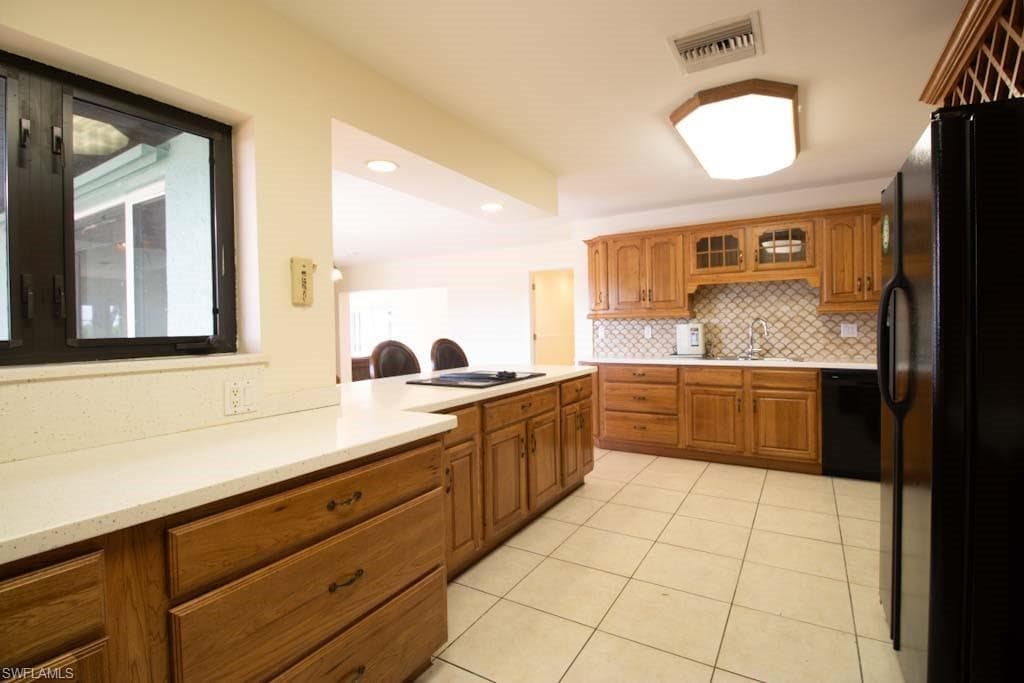 Kitchen with brown cabinets, black appliances, light tile patterned floors, and recessed lighting