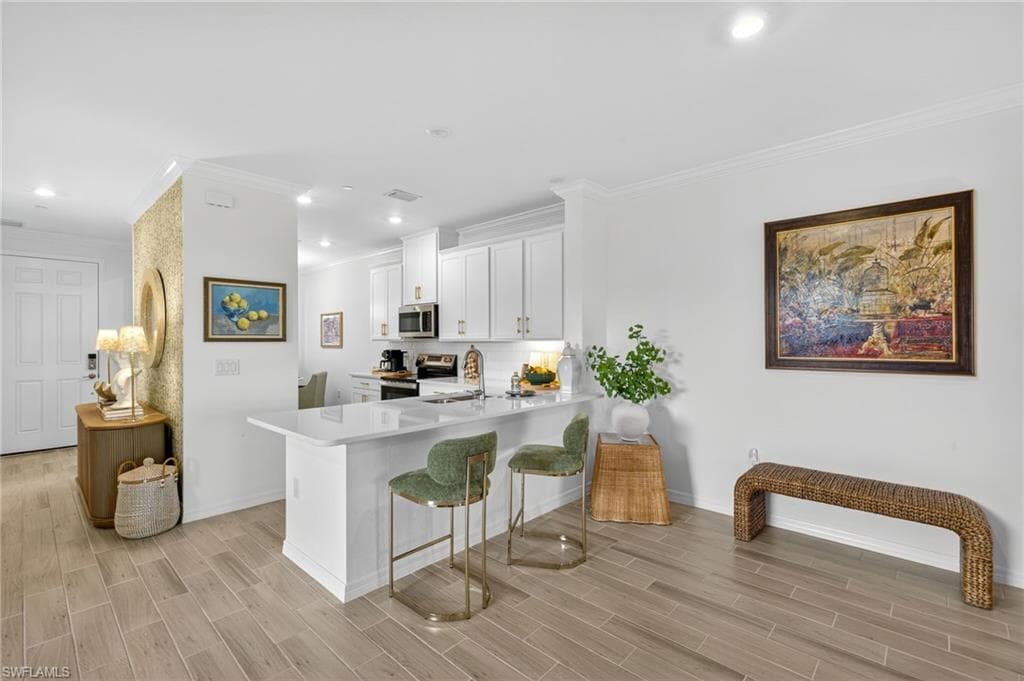 Kitchen featuring crown molding, a breakfast bar, wood finish floors, white cabinetry, and a peninsula