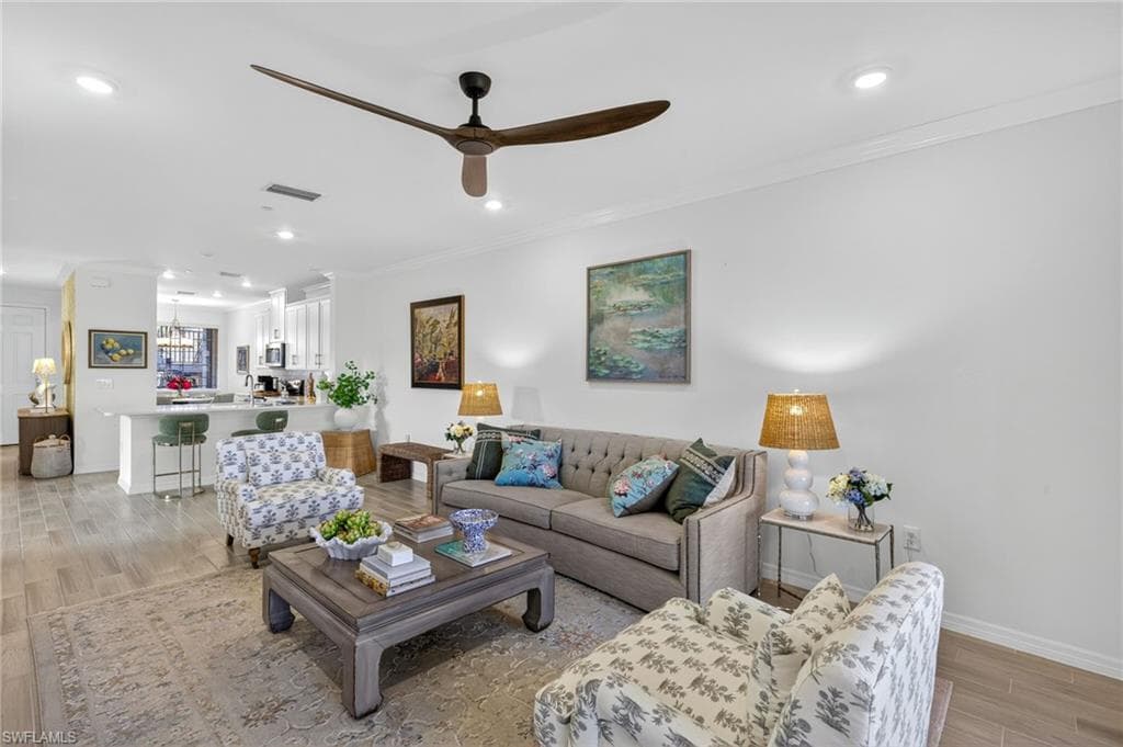 Living room featuring light wood-style floors, ornamental molding, a ceiling fan, recessed lighting, and a chandelier