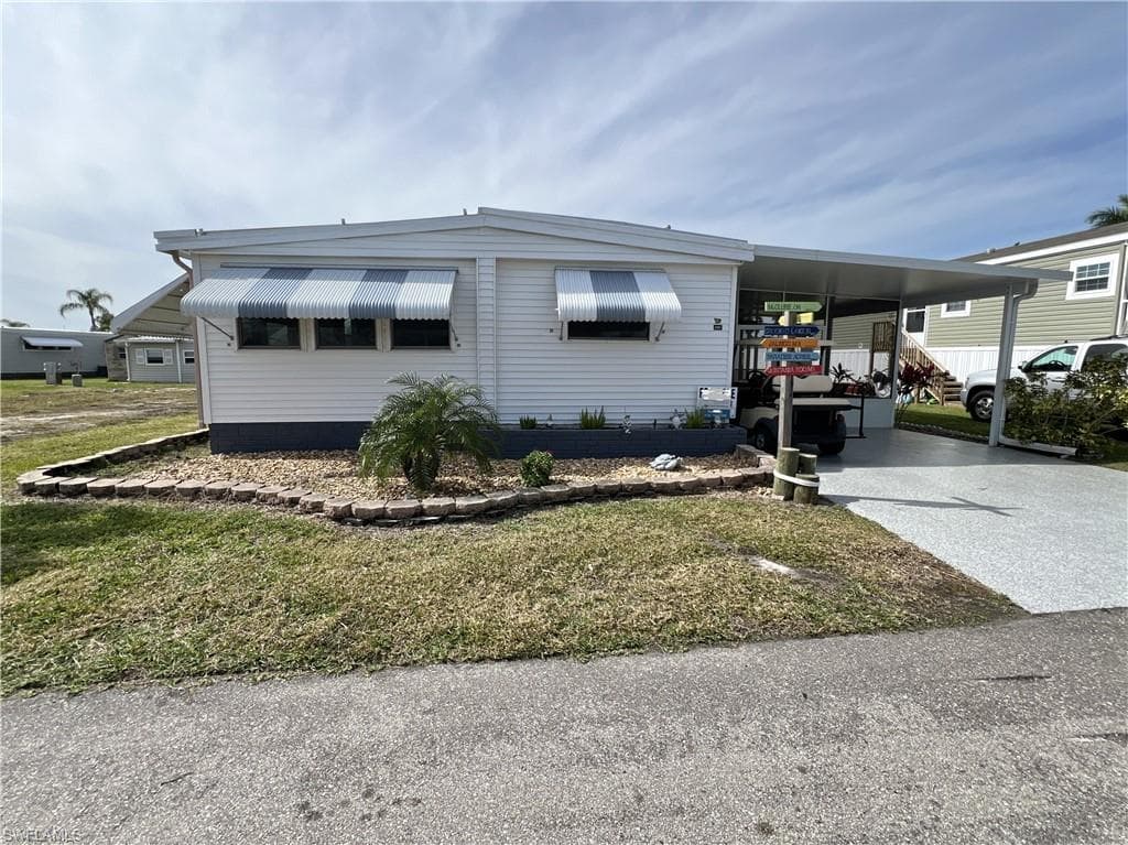 Manufactured / mobile home featuring a carport, concrete driveway, a front yard, and enclosed/covered lanai.