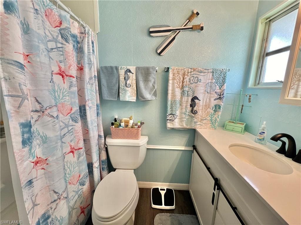 Full bath featuring a textured wall, vanity, dark wood-style floors, and curtained shower