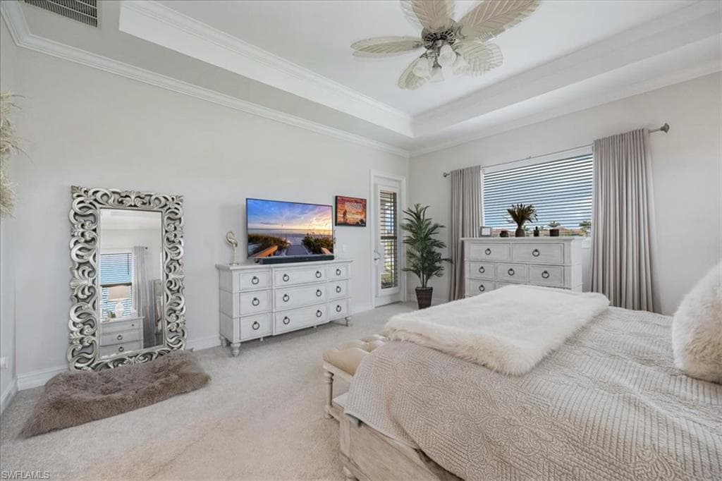 Bedroom with a tray ceiling, crown molding, light colored carpet, access to exterior, and a ceiling fan