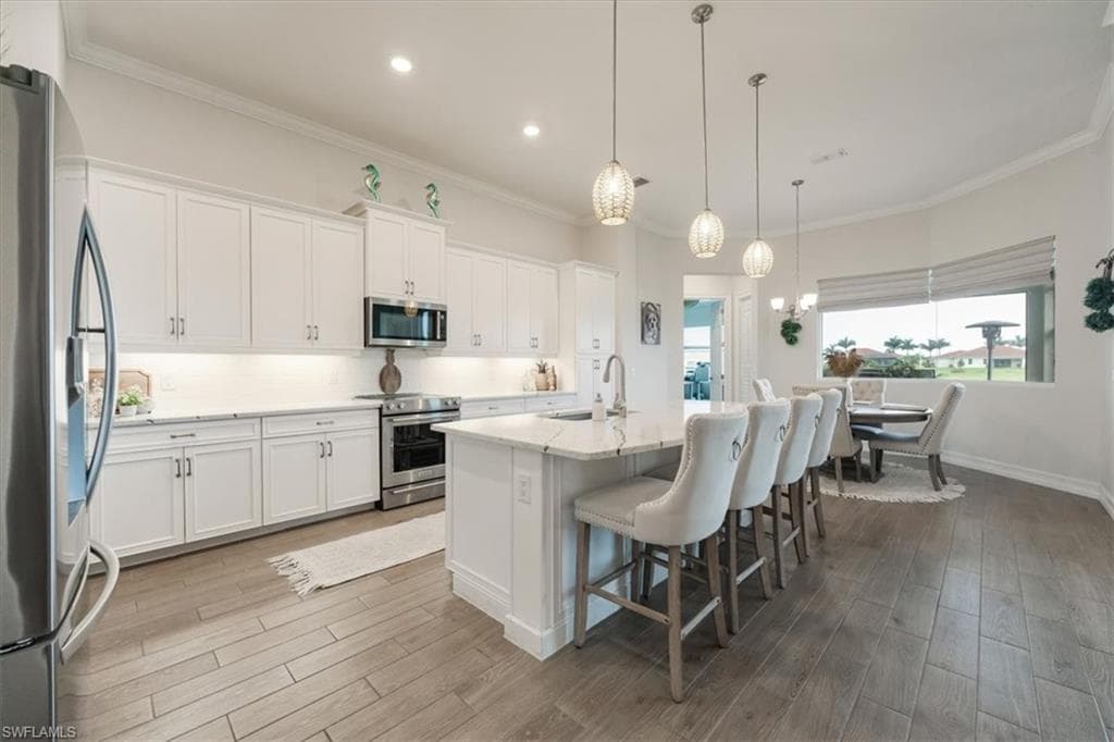Kitchen with tasteful backsplash, a breakfast bar, white cabinetry, crown molding, and appliances with stainless steel finishes