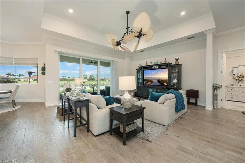 Living room with light wood-type flooring, crown molding, a raised ceiling, and recessed lighting