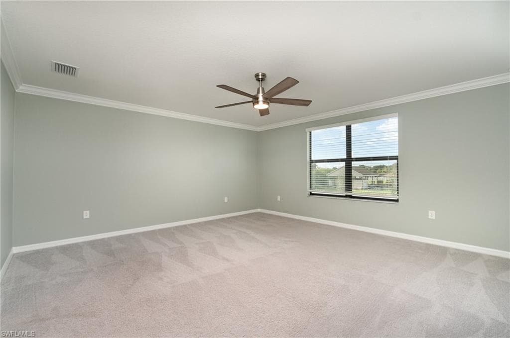 Empty room with ornamental molding, light carpet, and a ceiling fan